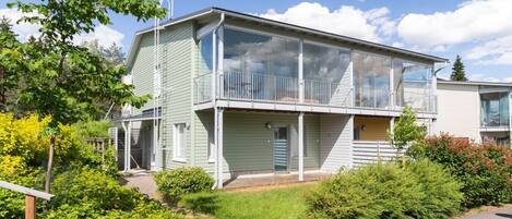 Un immeuble résidentiel à deux étages, doté d’un balcon, d’un garage dont la porte est bien visible et d’un jardin bien entretenu.