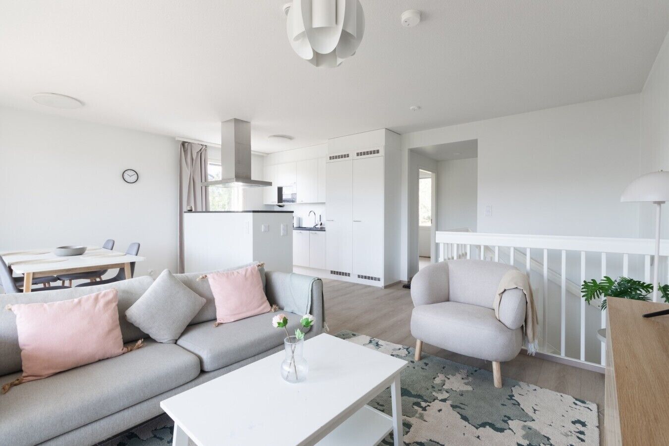 A modern living room with a grey sofa, a white coffee table, and a dining area with a table and chairs.