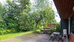 Un patio con una mesa y sillas, rodeado por un jardín con árboles y una valla de madera.