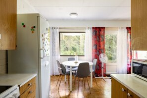Cozinha compacta com área de refeições, geladeira, micro-ondas e janela com cortinas.