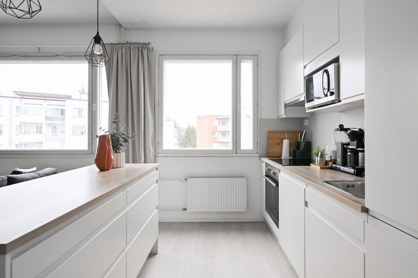 Moderni keittiö, jossa on valkoiset kaapit, puinen työtaso, sisäänrakennettu uuni ja ikkuna, jossa on verhot.
