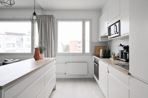 Eine moderne Küche mit weißen Schränken, einer Holz Arbeitsplatte, einem eingebauten Ofen und einem Fenster mit Vorhängen.