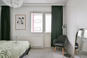 Une chambre à coucher avec un lit, une chaise, une lampe sur pied, une fenêtre avec des rideaux et un tableau encadré au mur.