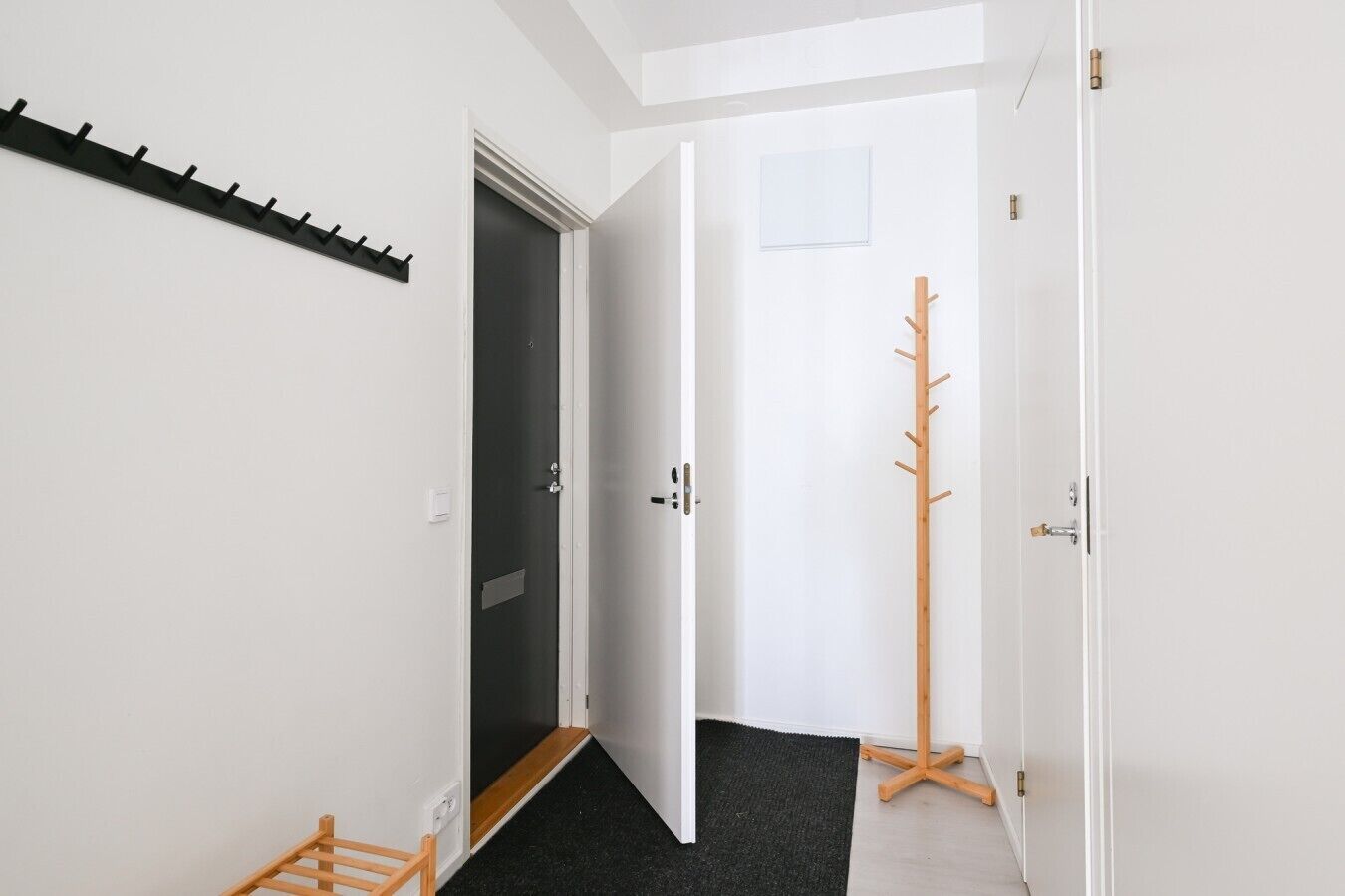 Un pasillo con un perchero, una puerta que da a un interior oscuro y un perchero de madera.