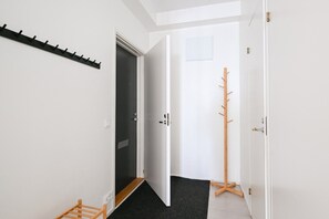 Ein Flur mit Kleiderhaken, einer Tür zu einem dunklen Innenraum und einem Holzständer für Kleidung.