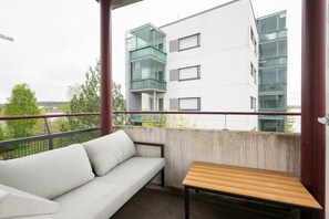 Un balcon avec un canapé blanc et une table en bois, donnant sur un immeuble moderne doté de nombreuses fenêtres.