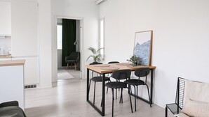 Interior moderno com área de jantar, mesa de madeira e cadeiras pretas, uma poltrona preta, planta em vaso e uma obra de arte emoldurada na parede.