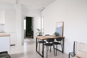Moderni sisustus, jossa on ruokailutila, jossa on puinen pöytä ja mustat tuolit, musta nojatuoli, ruukussa oleva kasvi ja seinällä oleva taideteos.