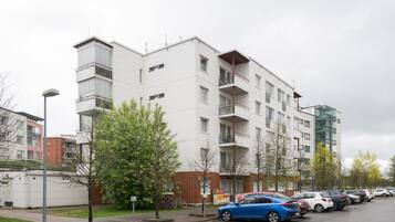 Kerrostalo, jossa on useita kerroksia, parvekkeita, parkkipaikka ja katulamppu.