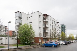 Kerrostalo, jossa on useita kerroksia, parvekkeita, parkkipaikka ja katulamppu.