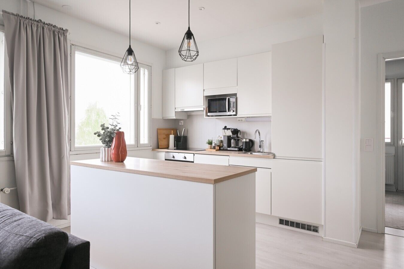 A modern kitchen with white cabinetry, a central island, a microwave, and pendant lighting.