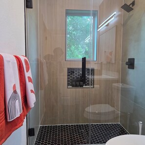 Un bagno moderno con box doccia in vetro, una finestra a vista e un portasciugamani con asciugamani decorati.