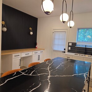 Una cucina moderna con isola in marmo nero, mobili bianchi e luci a sospensione.