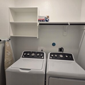 A laundry area with two white washing machines, a shelf with a box, and a power outlet. - Houston Oasis / Near Downtown• NRG • Med Ctr (Houston)