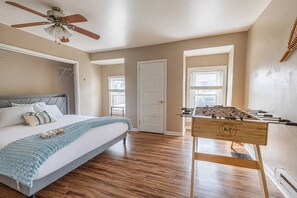A bedroom with a bed, a ceiling fan, a wooden foosball table, and a door. - Bright Mount Washington 3BR with Deck and Foosball (Pittsburgh)
