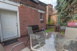 Eine Terrasse mit einem Glastisch, Metallstühlen, einem Grill und einer Backsteinmauer.