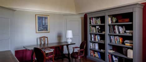 A study room with a wooden desk, two chairs, a bookshelf, and a framed picture on the wall.