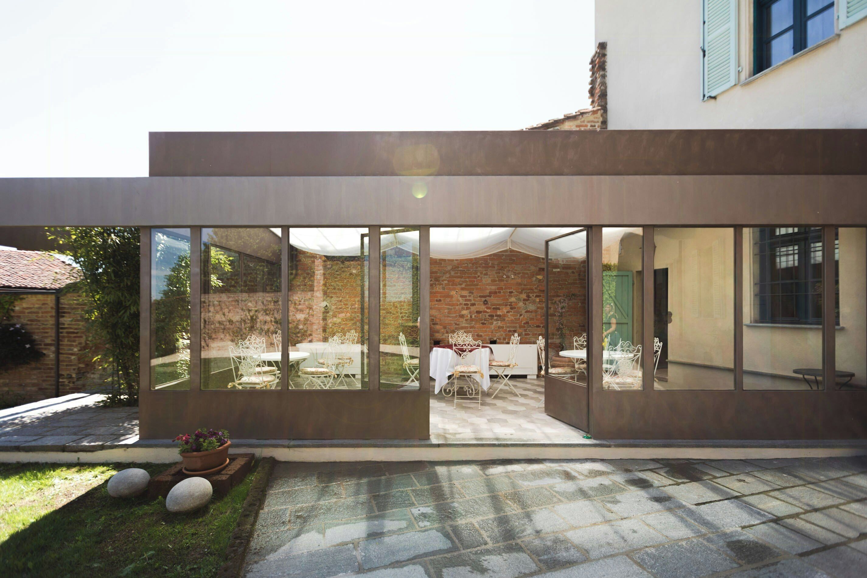 A modern building with large glass windows, a brick wall, and a courtyard with outdoor seating.