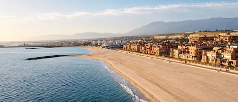 A coastal cityscape with a beach, buildings, and mountains in the background.