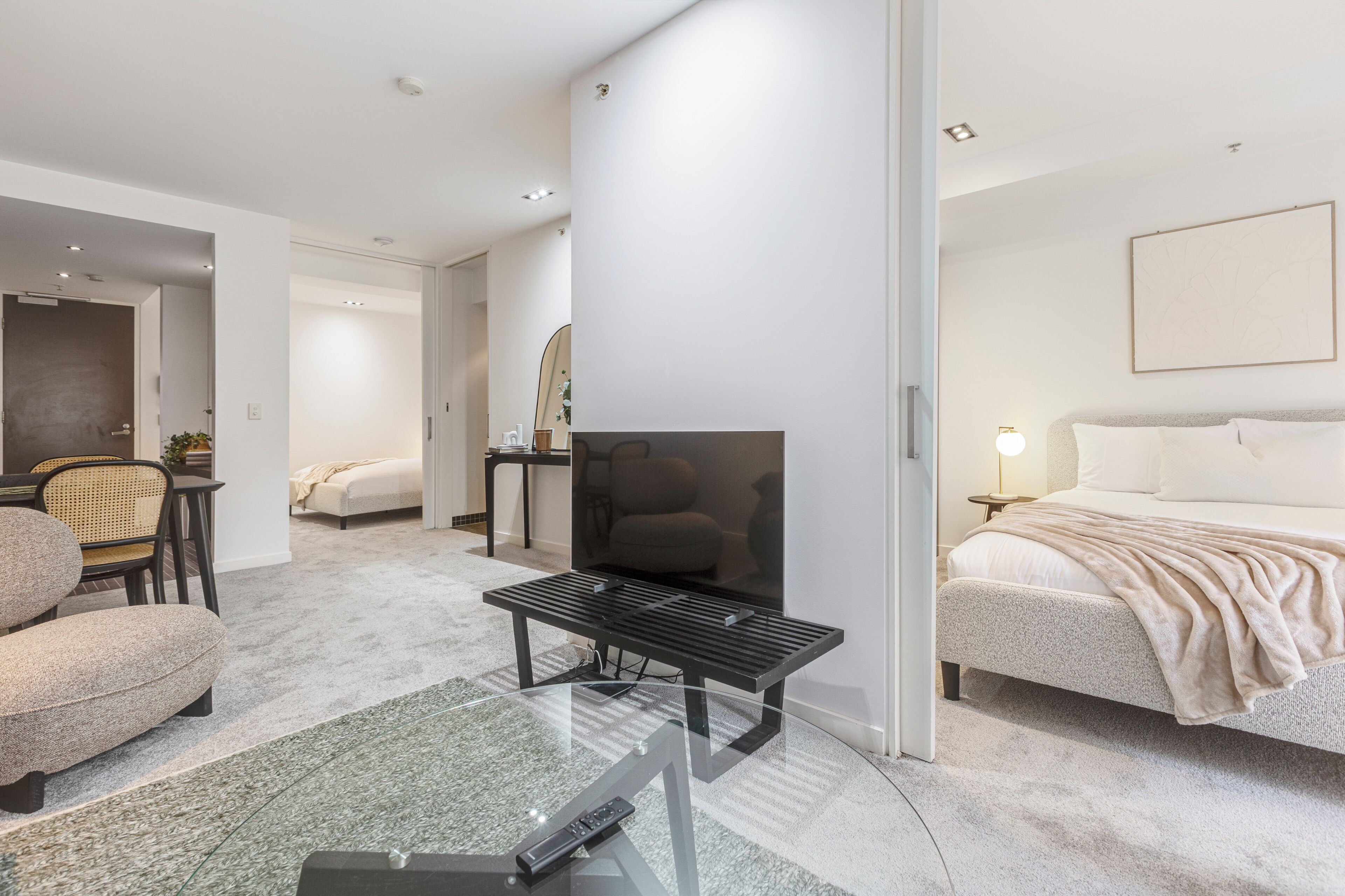 A modern hotel room with a glass coffee table, a bed, a sofa, a TV, and a painting on the wall.