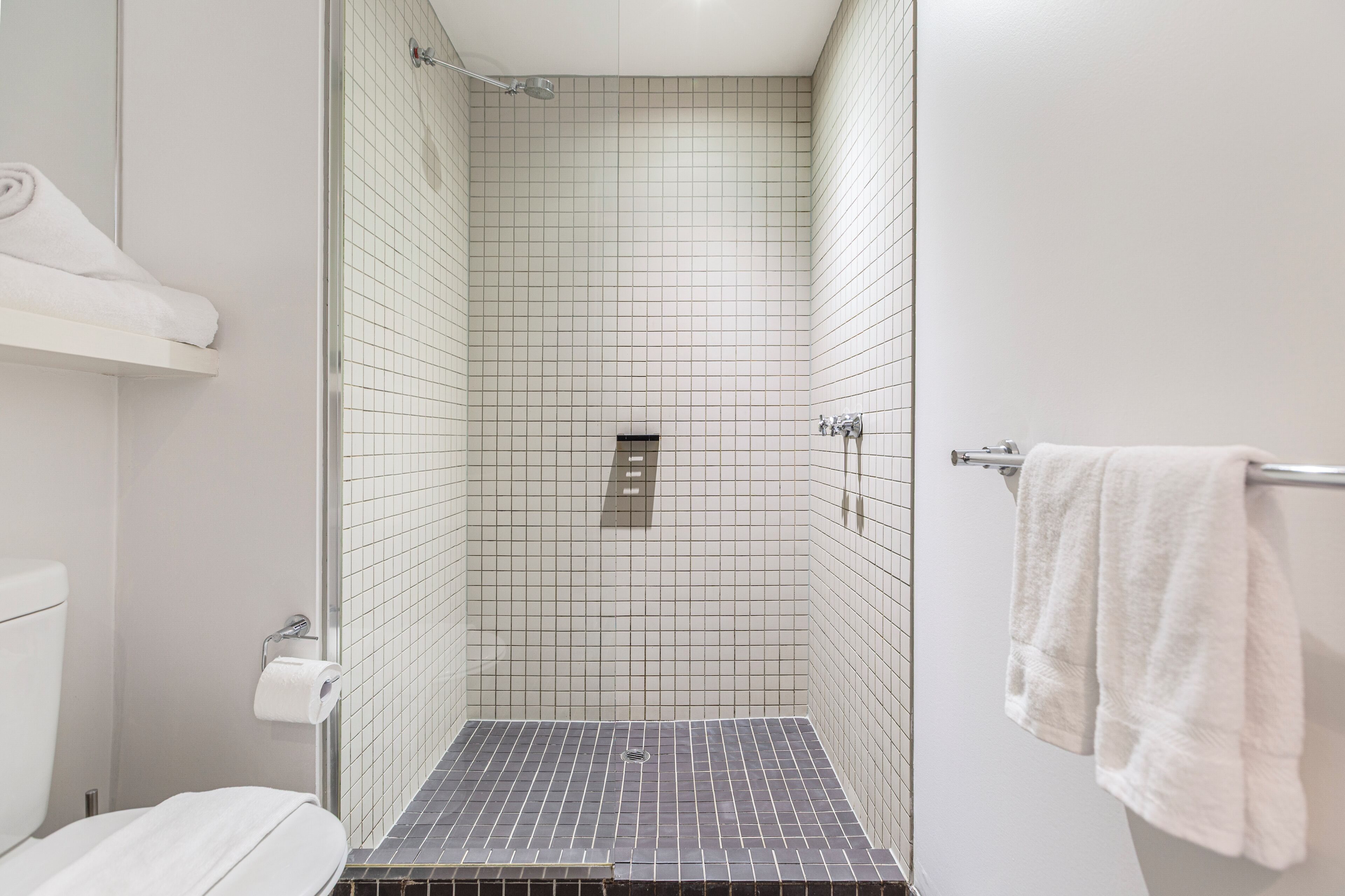 A modern bathroom with white tiled walls, a shower with a glass door, and a towel rack.