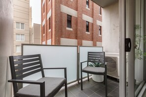 Ein Balkon mit zwei Stühlen, einem Blumentopf und Blick auf ein rotes Backsteingebäude.