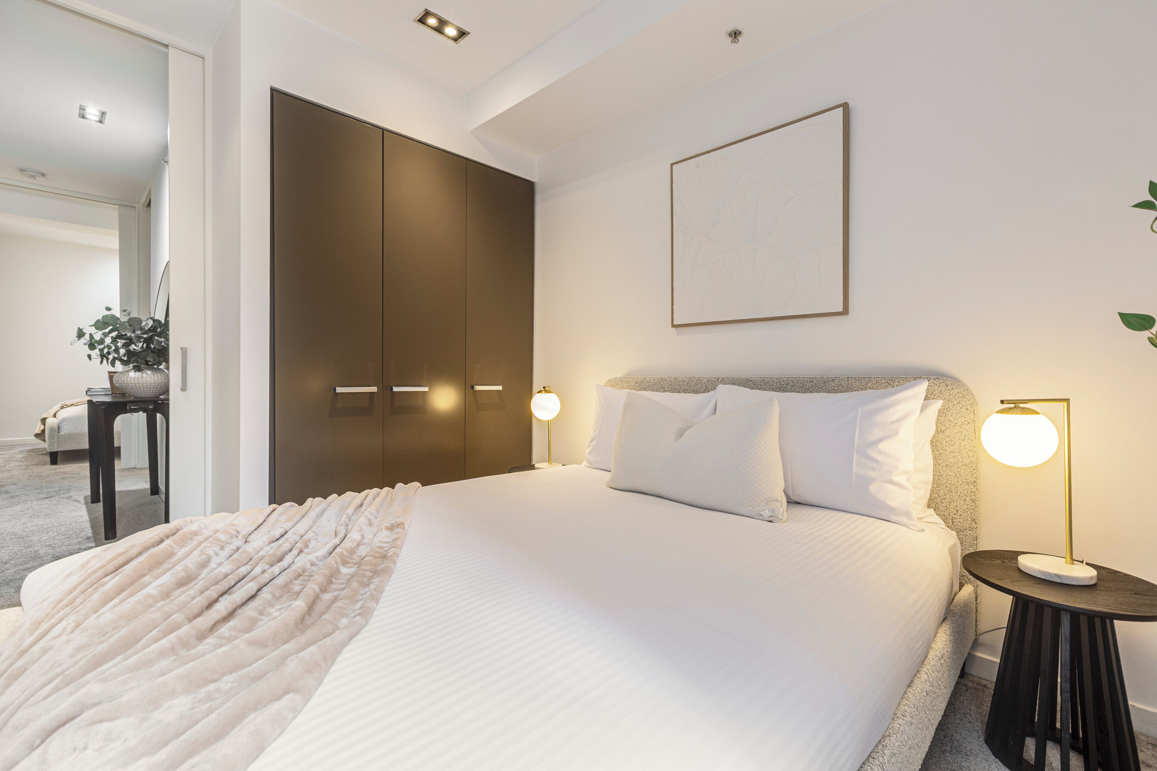 Ett hotellrum med en säng, sängbord, en garderob och en inramad tavla på väggen.