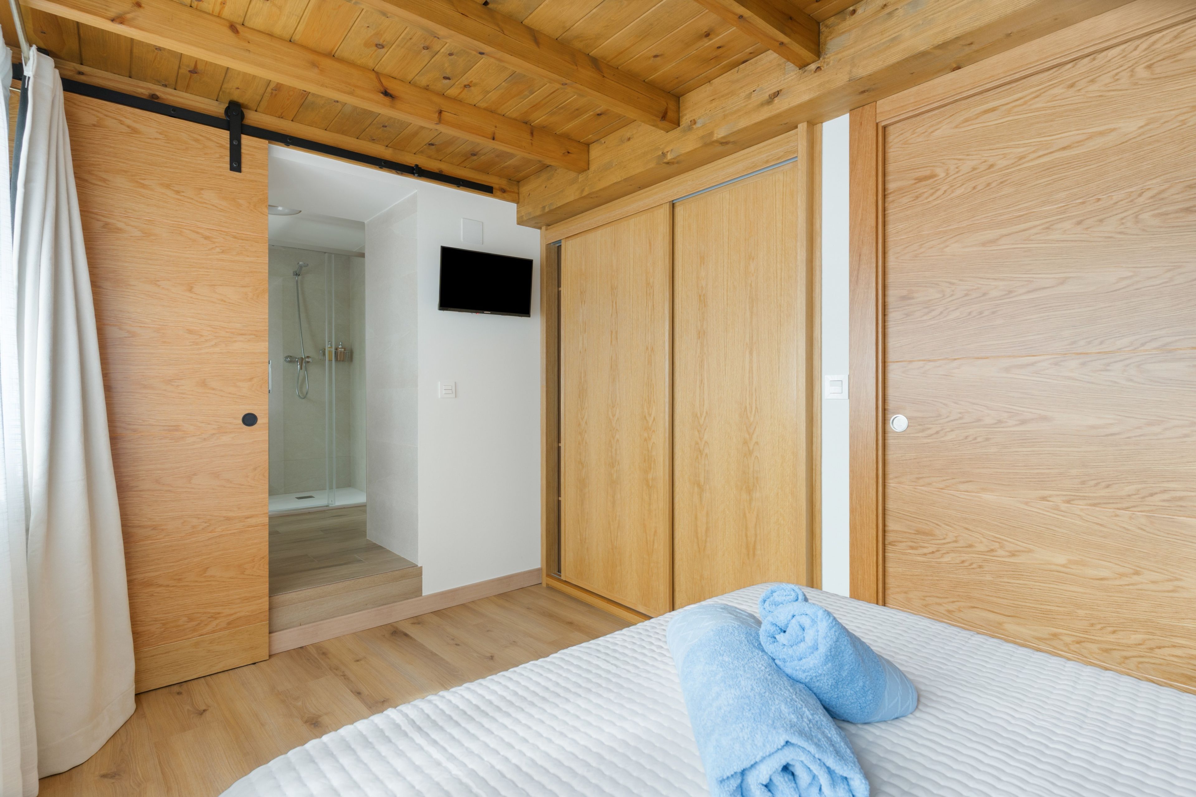Une chambre avec un plafond en bois, un lit avec une literie blanche, une armoire en bois et un espace douche.