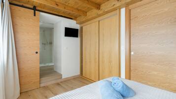 Ein Schlafzimmer mit Holzboden, einem Bett mit weißer Bettwäsche, einem Holzschrank und einem Duschbereich.