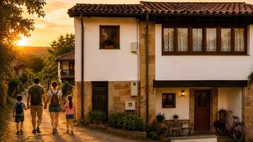A family walking down a dirt path towards a stone house with a tiled roof, a wooden door, and a bicycle parked outside.