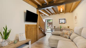 Una sala de estar moderna con techo de madera, un televisor de pantalla plana montado en la pared, un sofá con cojines estampados y un mueble de madera con un menú enmarcado.