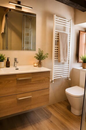 A modern bathroom with a wooden vanity, a mirror, a towel rack, a toilet, and a potted plant. - Holiday Home 'Vivienda Vacacional Casa Roque' with Private Terrace and Wi-Fi (Cangas de Onís)