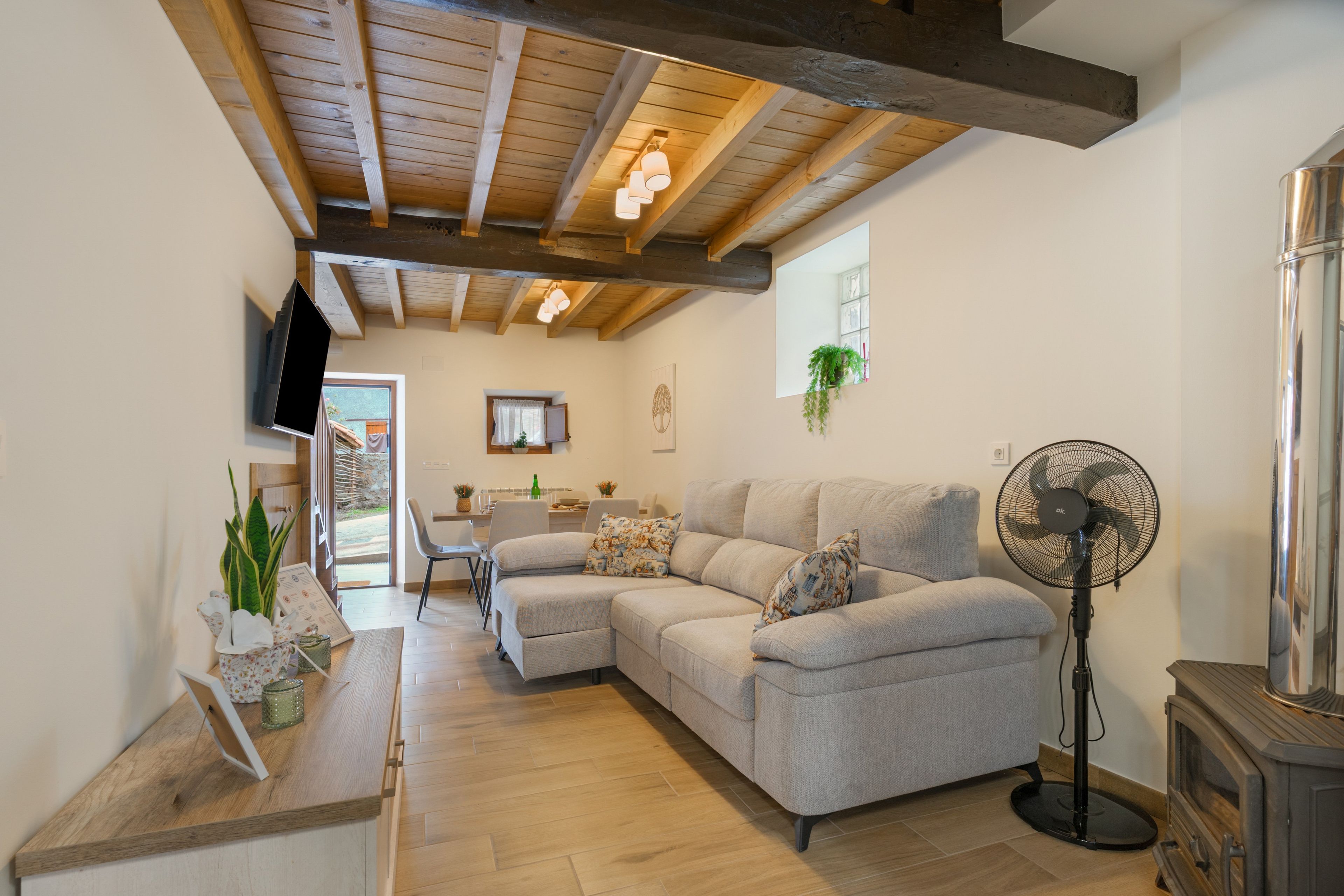 Een moderne woonkamer met een hoekbank, een staande ventilator en een houten plafond.