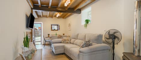 A modern living room with a sectional sofa, a standing fan, and a wooden ceiling.