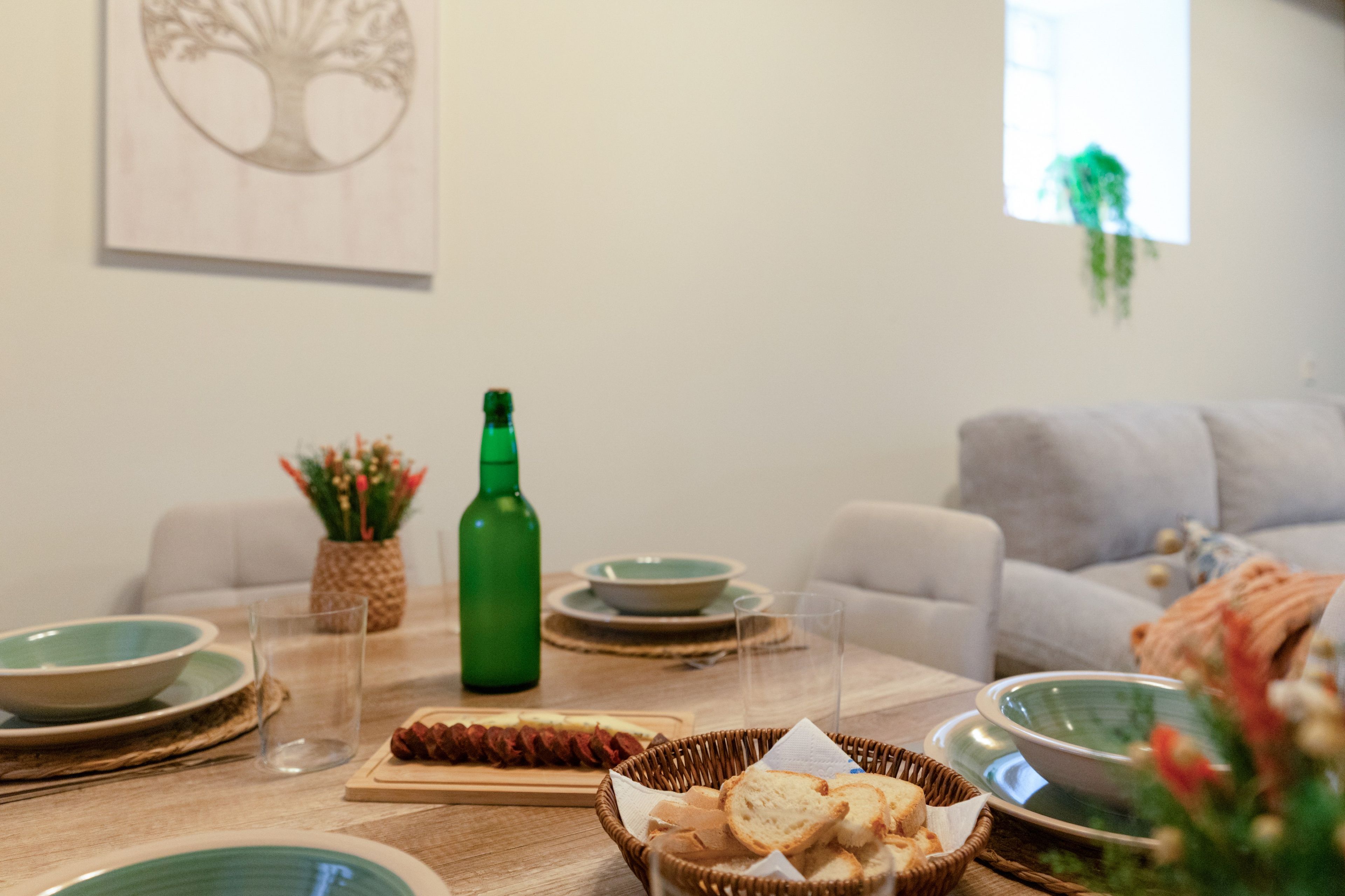 Une table à manger avec des assiettes, des verres, une bouteille et un panier de pain.