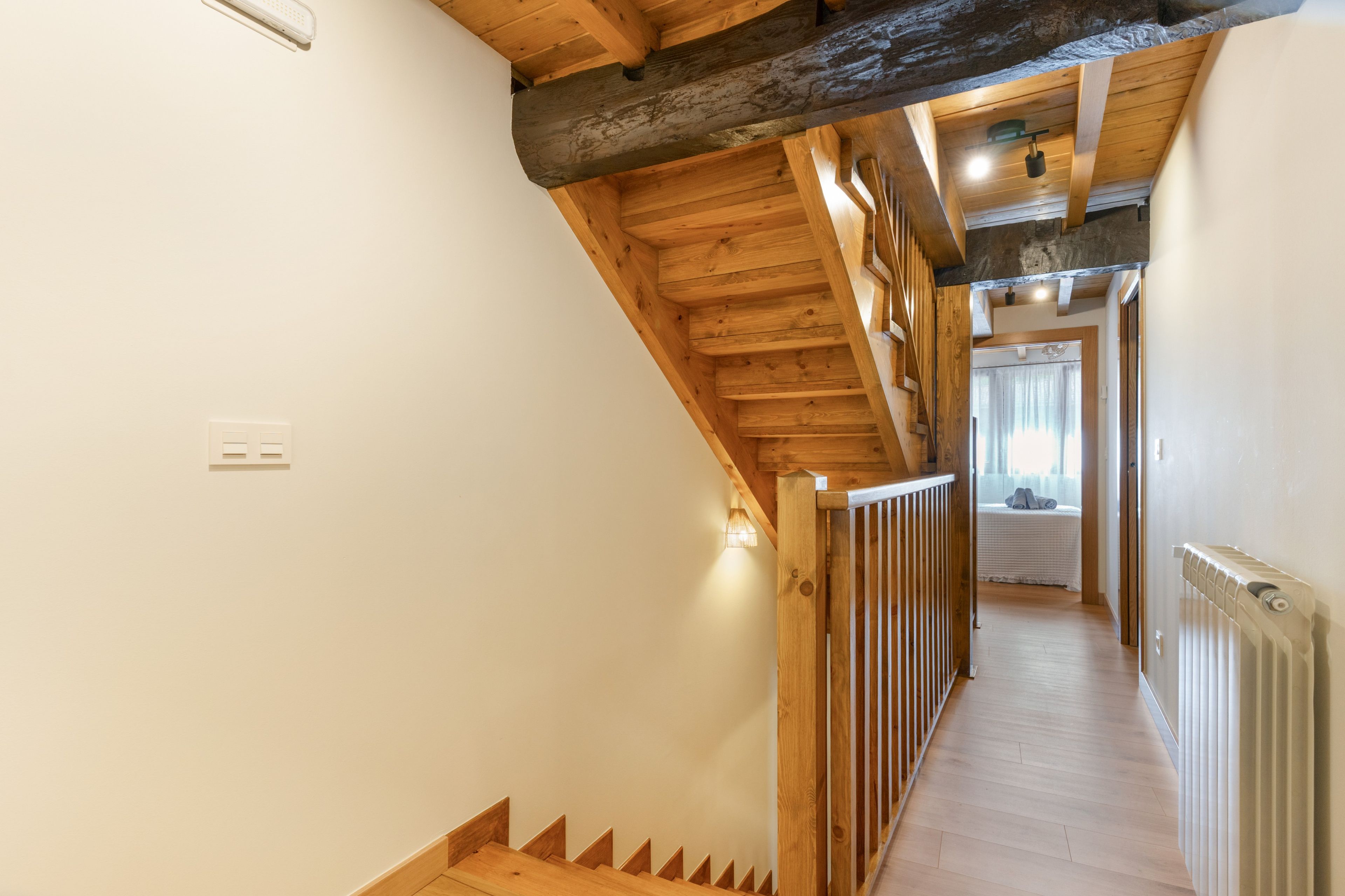 Una escalera de madera con barandilla que lleva a un dormitorio con cama y radiador.