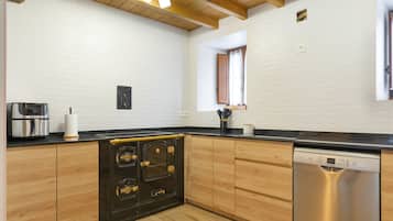 Una cuina amb armaris de fusta, un fogó negre, un rentaplats Bosch i una paret de maó blanc.