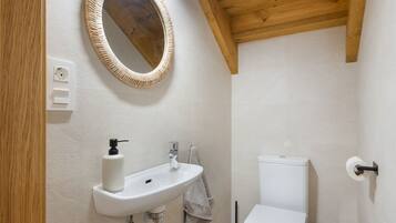 Een badkamer met een houten plafond, een ronde spiegel, een witte wasbak, een toilet en een handdoek aan de muur.