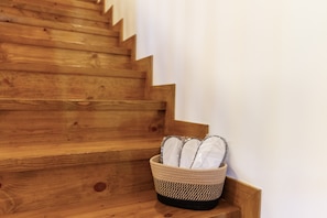 A wooden staircase with a woven basket containing white slippers at the bottom.