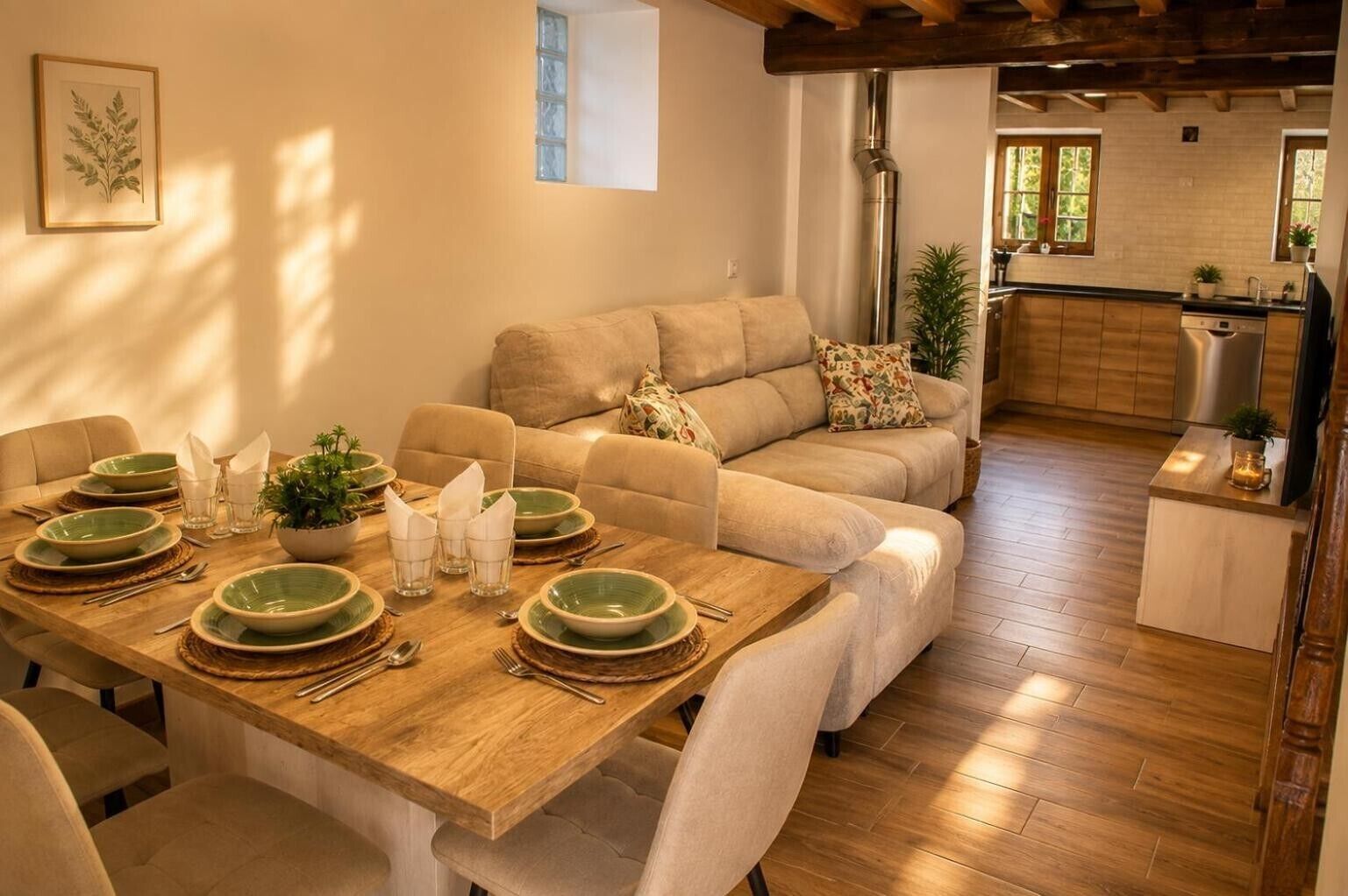 A dining area with a wooden table set for four, a sofa, and a kitchen in the background.