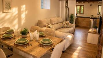 A dining area with a wooden table set for four, a sofa, and a kitchen in the background.