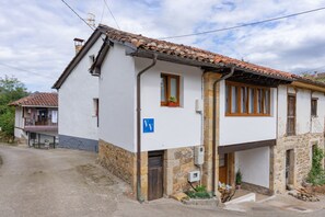 A two-story building with a tiled roof, a visible entrance, and a small garden area with plants.