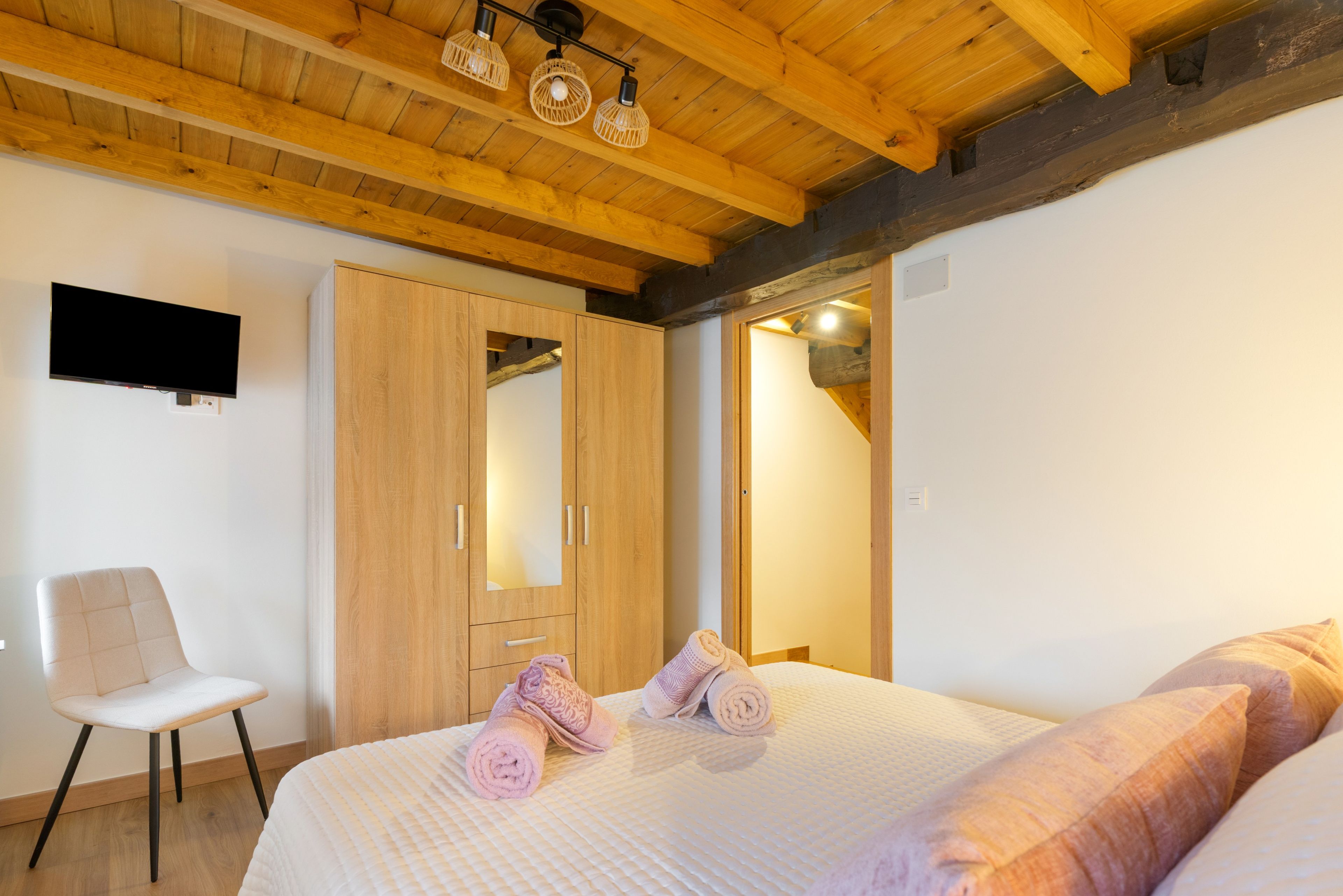 Een slaapkamer met een bed, een stoel, een kledingkast en een televisie aan de muur.