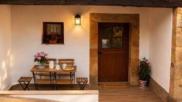 A wooden bench and table set up on a porch with a welcome mat, a potted plant, and a door with a window.