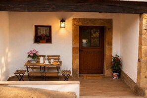 A wooden bench and table set up on a porch with a welcome mat, a potted plant, and a door with a window. - Holiday Home 'Vivienda Vacacional Casa Roque' with Private Terrace and Wi-Fi (Cangas de Onís)