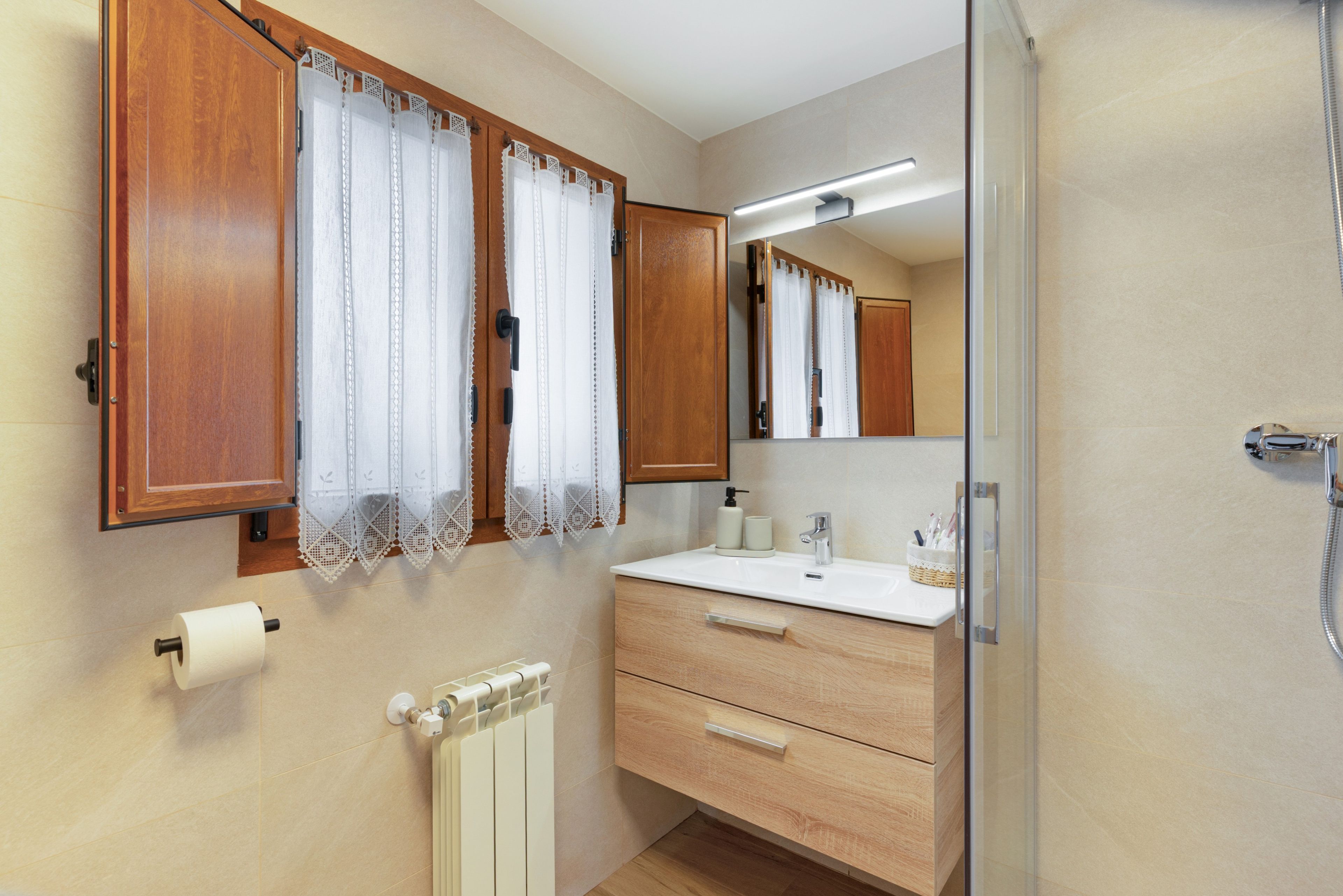 Un baño con armarios de madera, un lavamanos blanco, un espejo y un dispensador de papel higiénico.