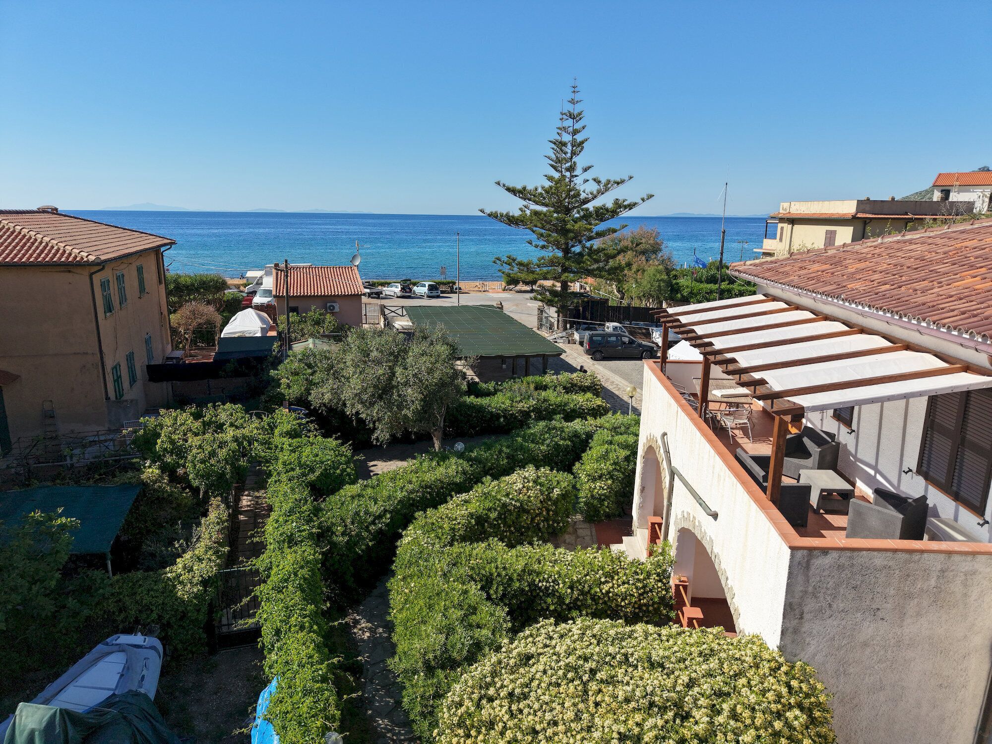 A coastal property with a view of the sea, a garden with various plants, and a building with a tiled roof.
