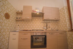 A kitchen with wooden cabinets, a built-in oven, and a patterned backsplash. - Margherita-3 by Appartamenti Margherita seafront accommodation in Giglio Campese (Giglio Campese)