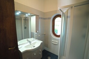 Un bagno con lavandino, specchio, doccia e finestra.