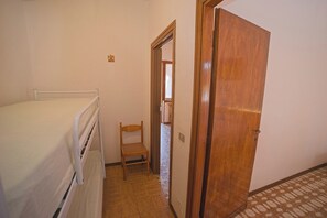 A narrow hallway with a bed on the left, a wooden chair in the center, and a wooden door on the right. - Margherita-3 by Appartamenti Margherita seafront accommodation in Giglio Campese (Giglio Campese)